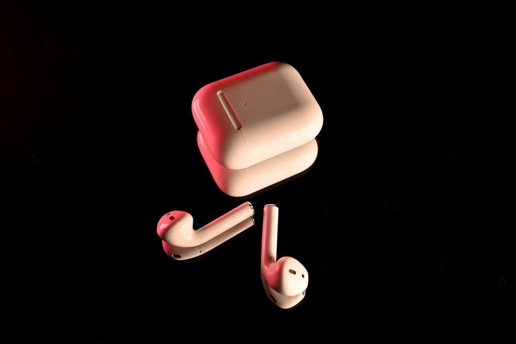 A pair of wireless earbuds glowing on a dark surface